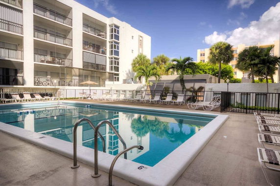 Front view of a multi-story building with balconies overlooking a swimming pool area.