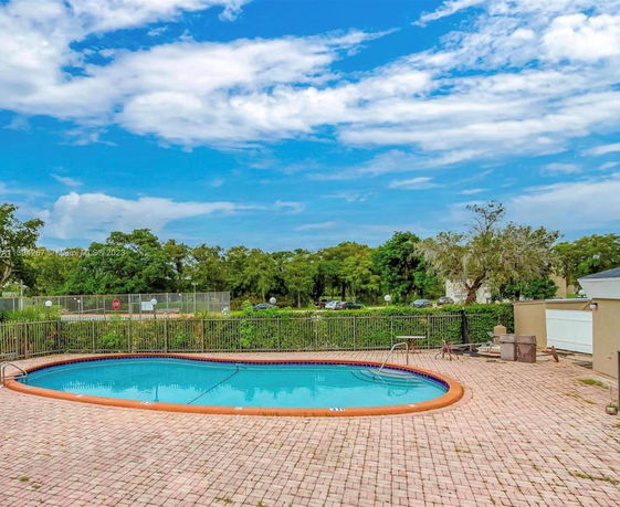 Outdoor swimming pool with surrounding brick patio and nearby greenery.