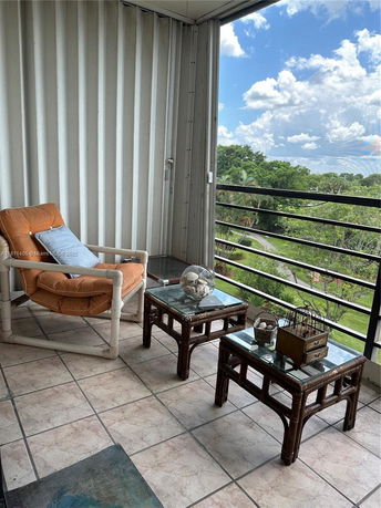 Balcony with seating and tables overlooking a lush green landscape.
