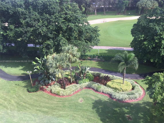 Aerial view of landscaped area with trees and pathways, surrounded by grassy fields.