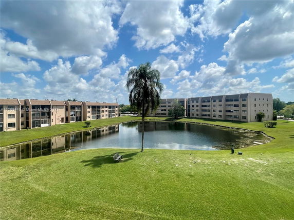 Multiple residential buildings overlooking a pond with grassy areas.