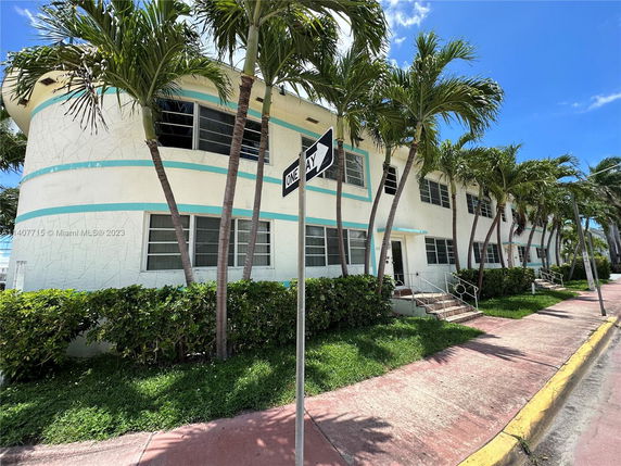 Front view of a two-story building with palm trees and a sidewalk.