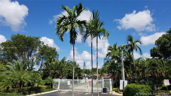 View of a gated area with palm trees and a house in the background.