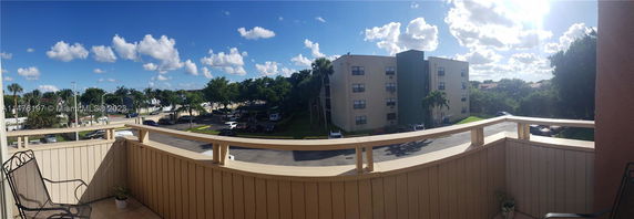 Panoramic view from a balcony overlooking a residential area with several apartment buildings and a parking lot.
