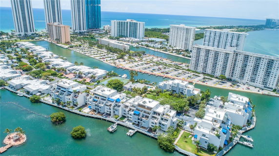 Aerial view of a waterfront residential area with multiple buildings and water channels, surrounded by high-rise apartments and a view of the ocean in the background.
