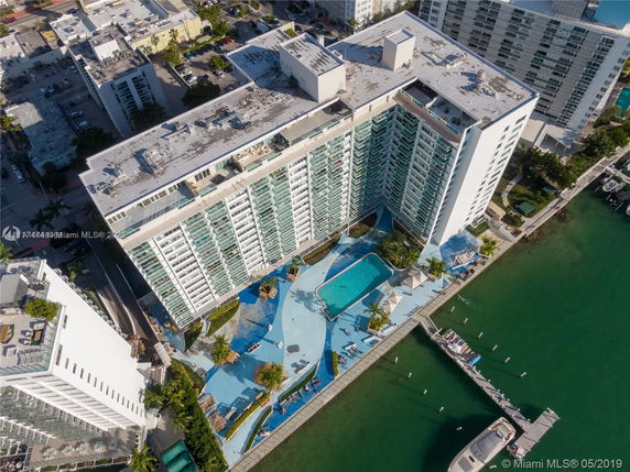 Aerial view of a large waterfront apartment complex with a central swimming pool area and dock.