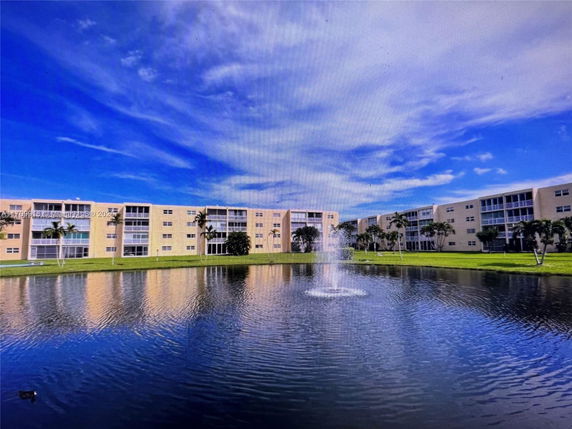 Front view of a multi-story apartment building with balconies, adjacent to a pond with a fountain.