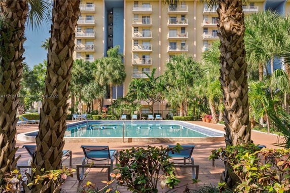 High-rise building with balconies, surrounded by palm trees and a pool area in the foreground.