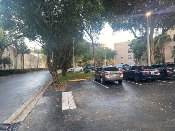 Outdoor parking area with several parked cars and surrounding trees.