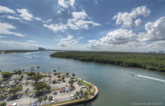 Panoramic view of a waterway with a boat, surrounded by greenery and a parking area in the foreground.