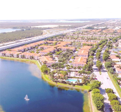 Aerial view of a residential area with orange-roofed buildings, adjacent to a body of water and a major highway.