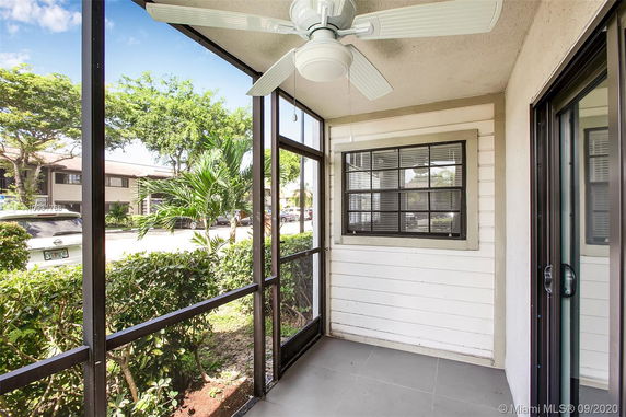 Enclosed porch area with ceiling fan and window view of a building and cars outside.