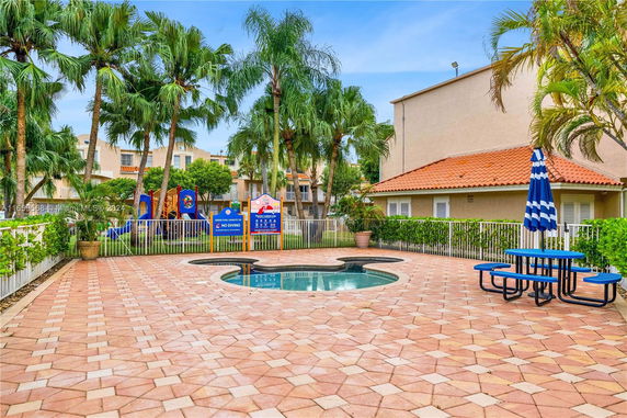 Outdoor play area with a small pool and playground equipment surrounded by palm trees.