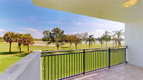 Balcony view overlooking a grassy area with palm trees and a body of water in the distance.