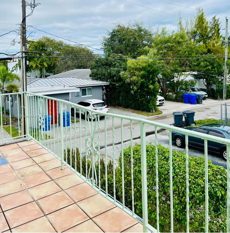 View from a balcony overlooking a residential street with parked cars and trees.