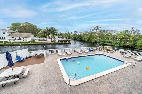 Outdoor area featuring a swimming pool with surrounding lounge chairs and a view of water and houses in the background.