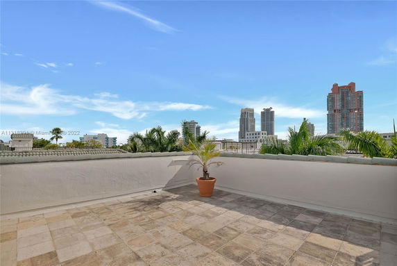 Rooftop area with tiled flooring and potted plant, offering a view of surrounding buildings.