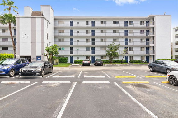 Front view of a multi-story residential building with a parking area in front.
