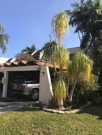 Front view of a house with a garage and palm trees.