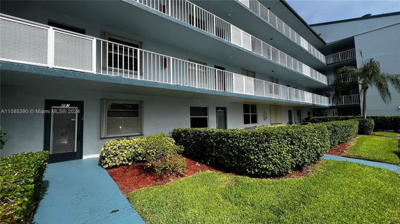 Front view of a multi-story residential building with balconies and a pathway lined with shrubs.