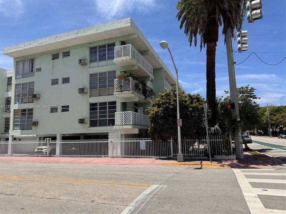 Front view of a multi-story building with balconies and a gated area at the ground level.