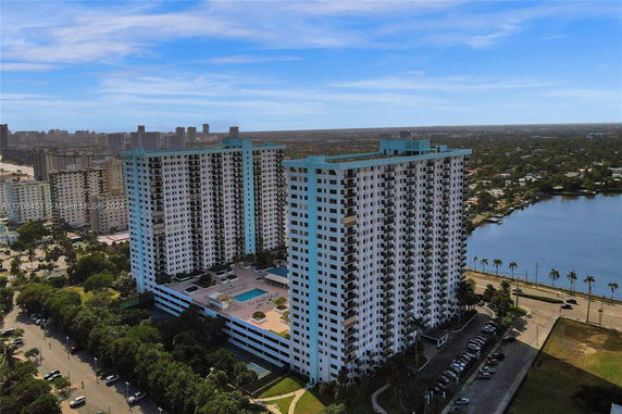 Aerial view of two tall residential buildings with balconies, adjacent to a body of water.