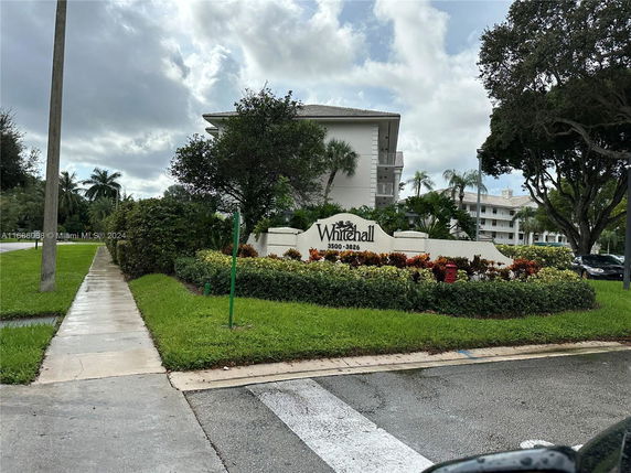 View of a multi-story residential building with signage indicating 'Whitehall,' surrounded by landscaping and trees.