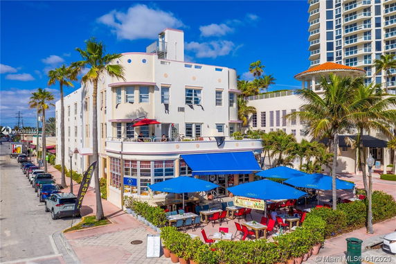 Front view of a multi-story building with outdoor seating area and blue umbrellas.