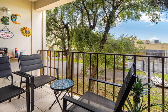 View from a balcony with outdoor chairs and decorative wall hangings, overlooking trees and nearby buildings.
