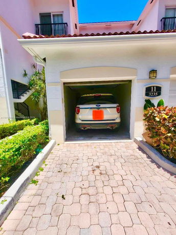 Outdoor parking area with a car parked in front of a garage of a two-story house.