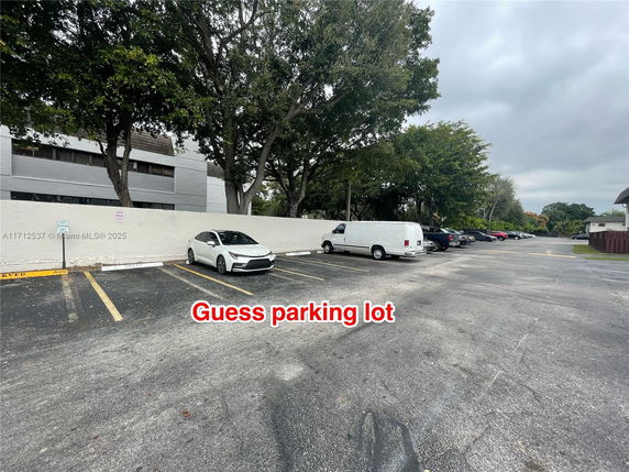 Outdoor parking area with several parked vehicles and surrounding trees.