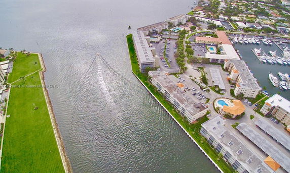 Aerial view of a waterfront complex with multiple buildings, a pool, parking areas, and a marina with boats.