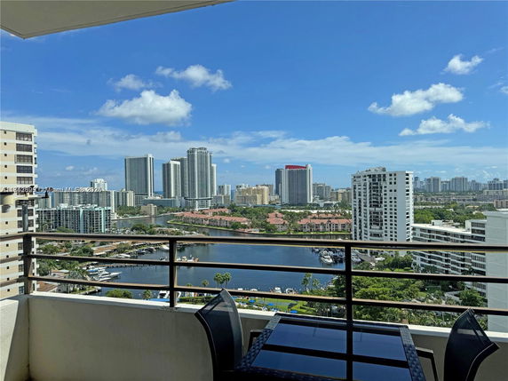 Panoramic view from a balcony showing a city skyline with high-rise buildings and a body of water.