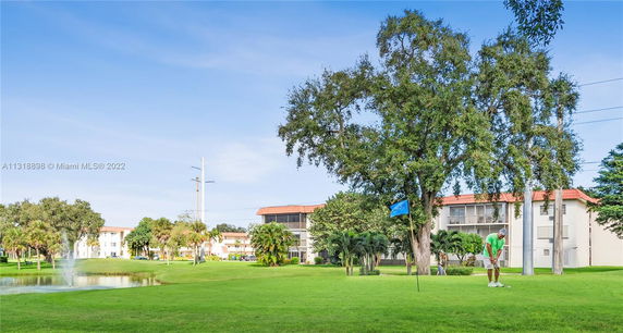 View of a multi-story residential building surrounded by trees and a pond.