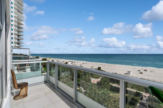 View from a balcony overlooking the beach and ocean, featuring a railing and a chair.