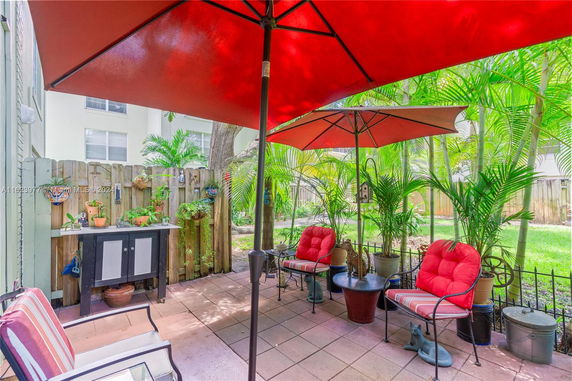 Outdoor patio area with chairs and umbrellas, surrounded by potted plants and a wooden fence.