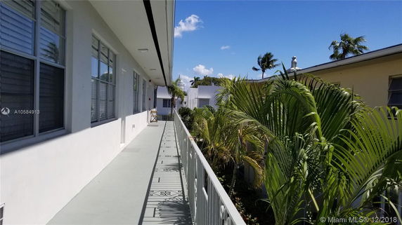 Exterior view of an apartment building with a walkway and tropical plants.