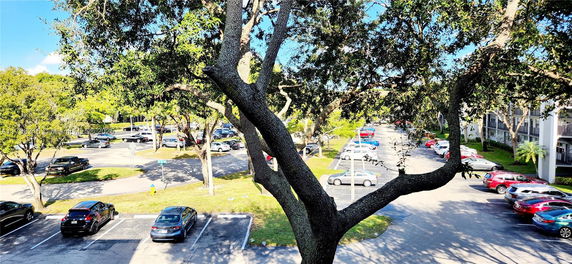 Image of an outdoor parking area with several cars parked under trees.