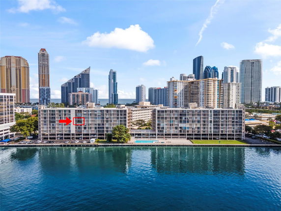 View of a multi-story building along waterfront with city skyline in the background.