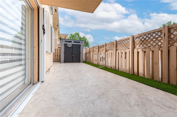 Outdoor area with tiled flooring, fenced boundary, and a small shed.
