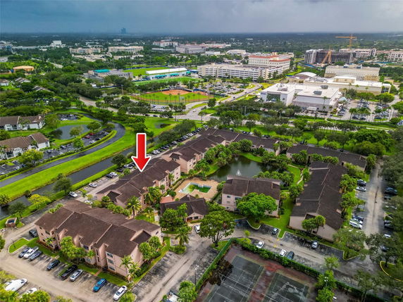 Aerial view of a residential area with multiple buildings and parking spaces, surrounded by greenery and roads.