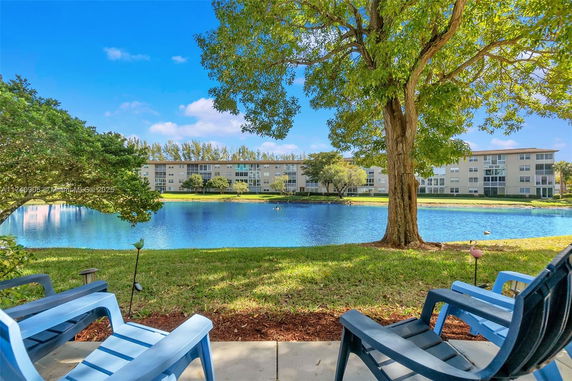 View of a building across a lake with trees and chairs in the foreground.