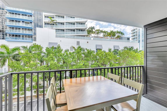 Balcony view overlooking modern buildings with lush greenery in the foreground.