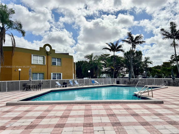 Outdoor swimming pool area with a fence and lounge chairs, adjacent to a building with a distinctive circular design element.