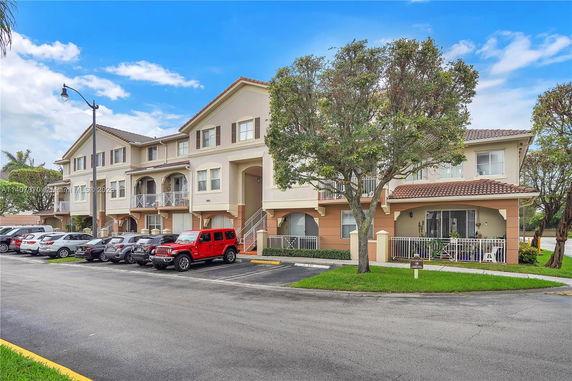 Front view of a three-story residential building with balconies and parked cars.