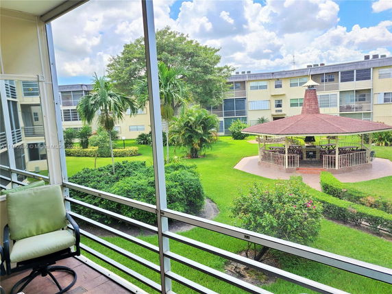 View of a courtyard garden area with a gazebo, surrounded by apartment buildings and palm trees.