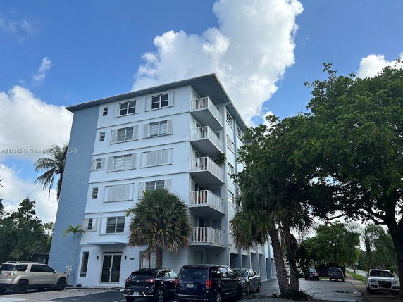 Front view of a multi-story residential building with balconies and parked cars in front.