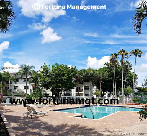 Outdoor swimming pool area with surrounding palm trees and buildings in the background.