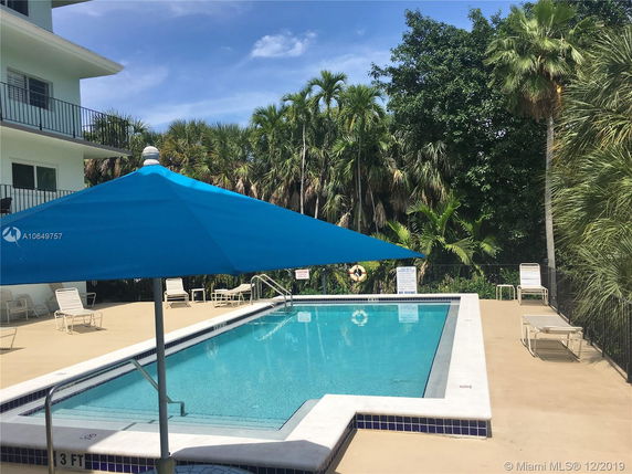 Pool view with a partially visible building and surrounding trees.