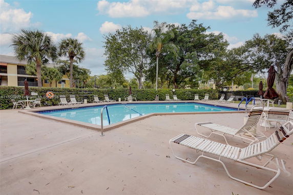 Outdoor swimming pool area with lounge chairs and surrounding foliage.